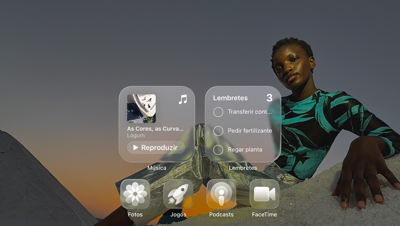 Tela em Liquid Glass com ícones de apps transparentes, como Apple Music, Lembretes, Fotos, Jogos, Podcasts e FaceTime, que criam um efeito de refração na imagem de fundo.