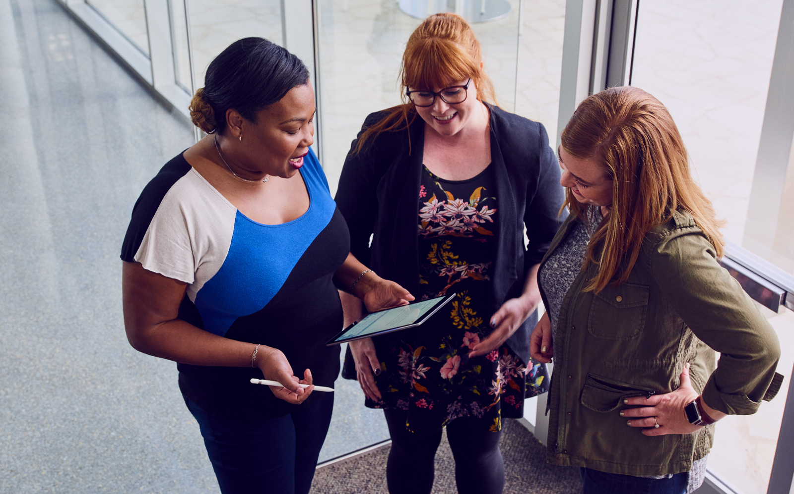 Three Apple Support Advisors are standing together in an Apple office, looking at an iPad and having a conversation.