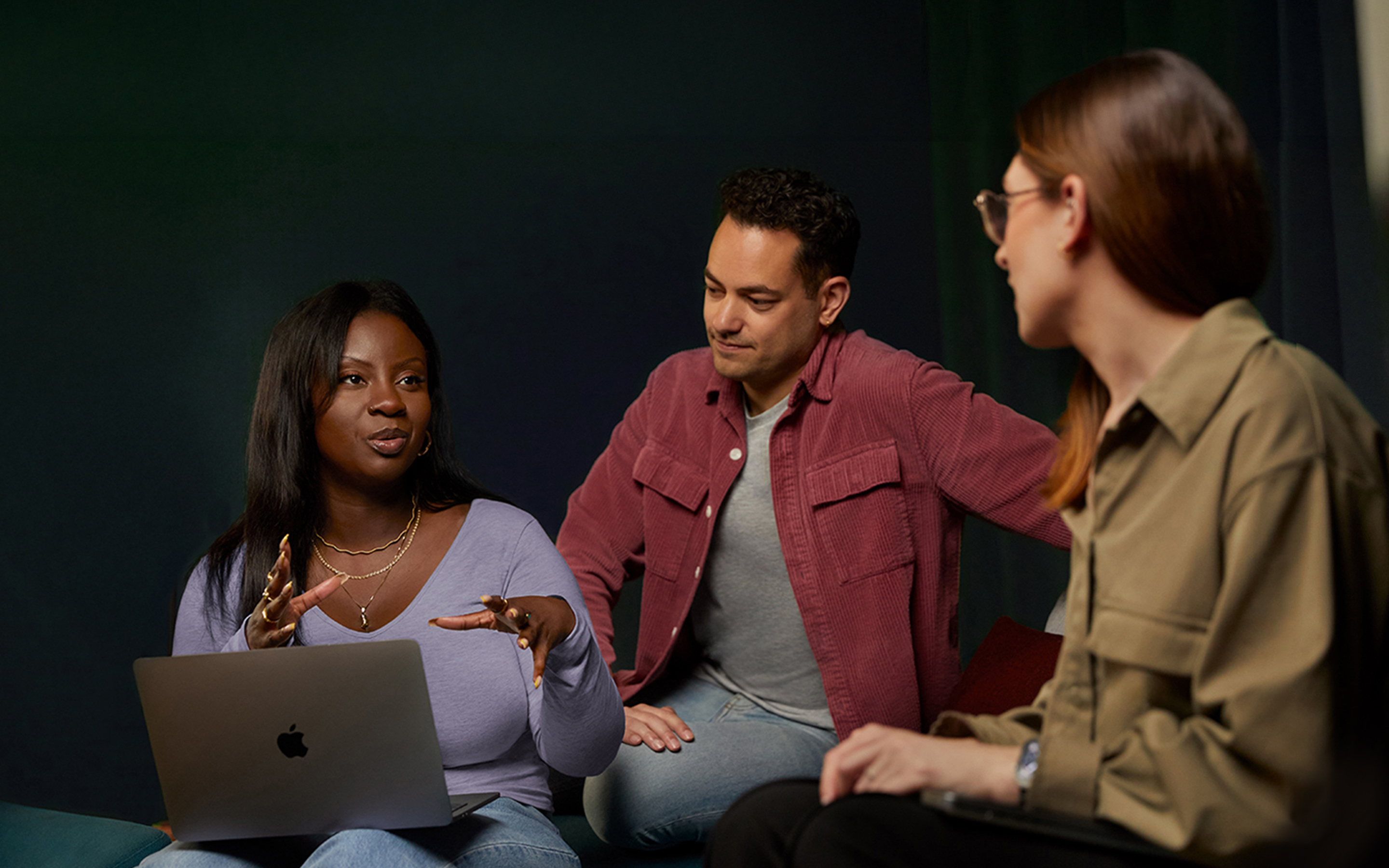 Trois membres de l’équipe Logiciels et services d’Apple discutent sur un canapé. Une des personnes tient un MacBook.