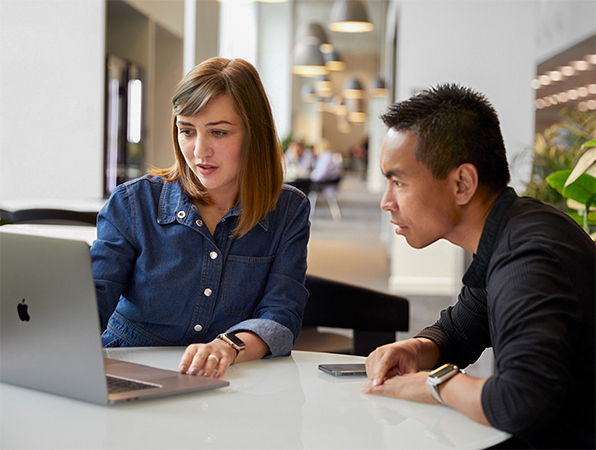 Two Apple Support and Service team members looking at a MacBook in a common area.