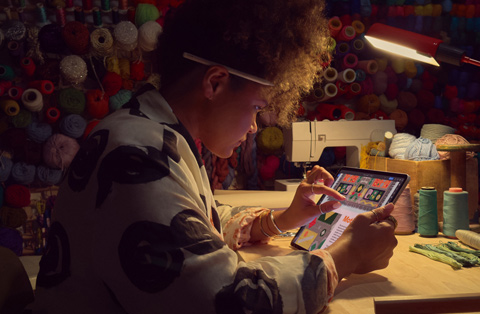 A person sitting at a desk uses two fingers on the screen of an iPad to zoom in on an image.