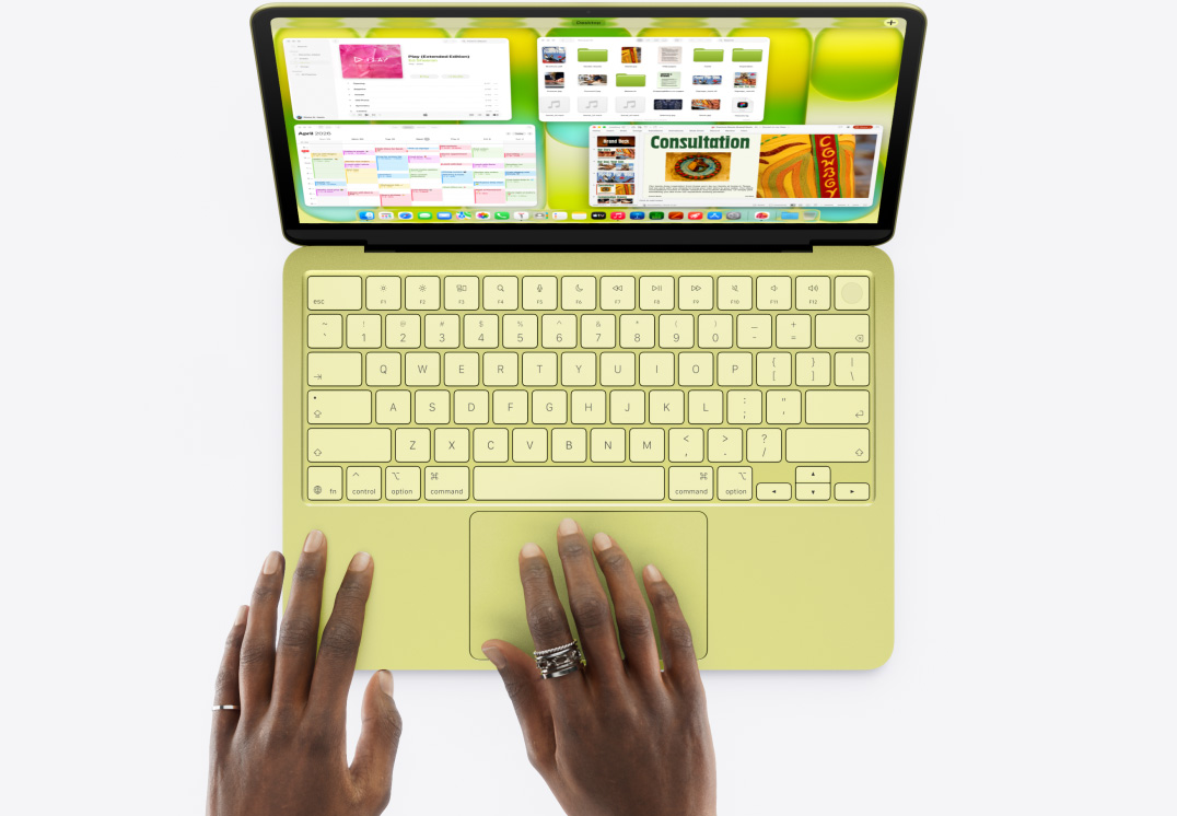 MacBook Neo, citrus colour, a person's hand on trackpad, multiple windows open including Music, Calendar and Microsoft PowerPoint apps