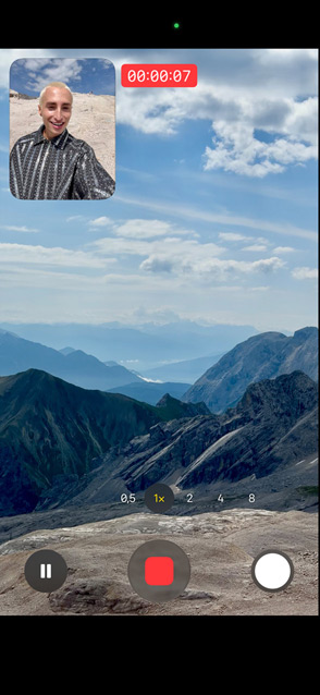 Une personne montre la vidéo double capture en s’enregistrant avec la caméra avant, tout en filmant des montagnes à l’arrière-plan avec la caméra arrière