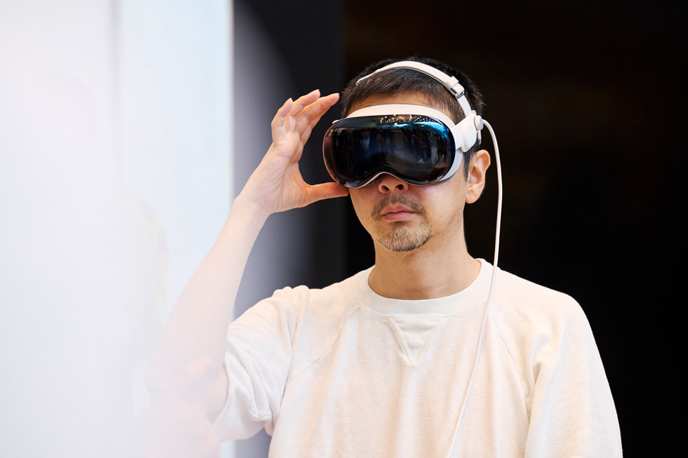A customer wearing Apple Vision Pro holds a hand up next to his head inside Apple Omotesando.