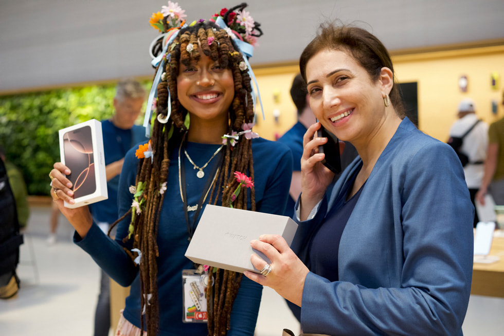 Une employée souriante et tenant une boîte d’iPhone 16 Pro se tient à côté d’une cliente tenant une boîte d’Apple Watch à Apple Fifth Avenue, à New York.
