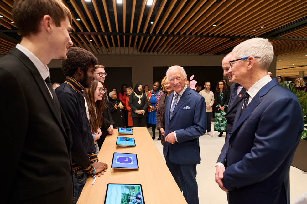 Le roi Charles et Tim Cook rencontrent des anciens élèves du King’s Trust, qui se tiennent derrière une table avec des iPad.