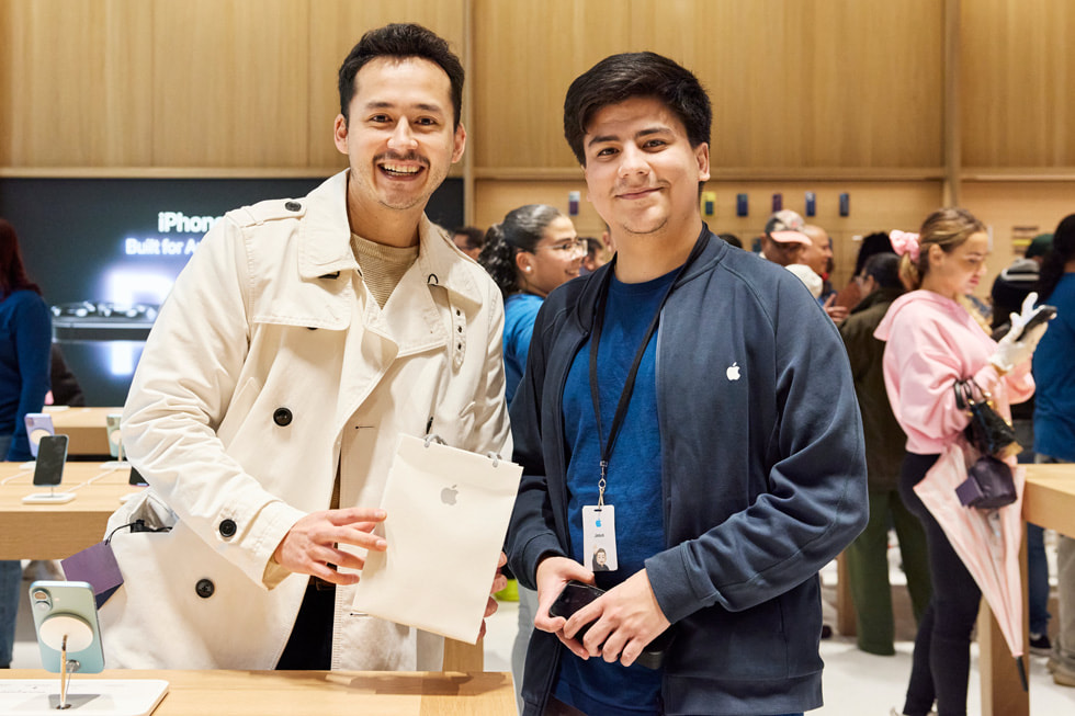 A customer holding an Apple bag stands next to an Apple team member at Apple Miami Worldcenter.
