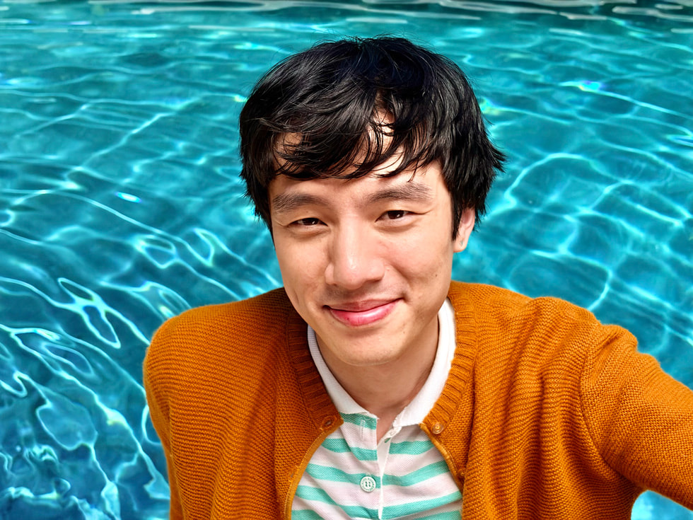 A portrait taken with iPhone 17 features a subject standing in front of colorful foliage.