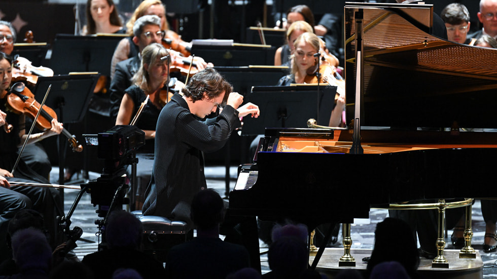 An image of pianist Lukas Sternath on stage at a live performance with an orchestra in the background.