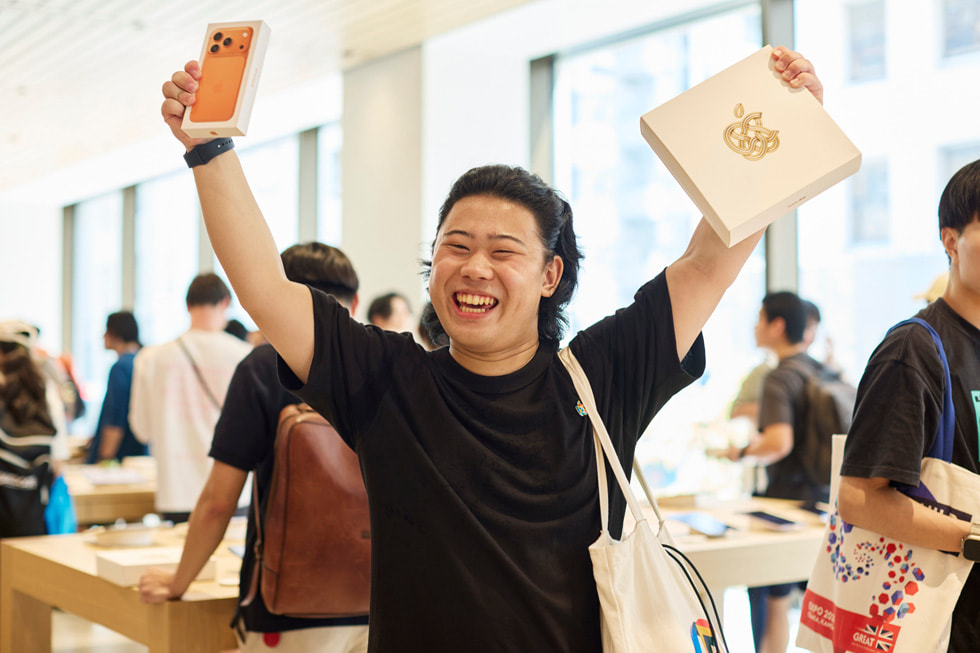 A customer is shown holding iPhone 17 Pro in cosmic orange in one hand and a commemorative Apple Ginza gift in the other.