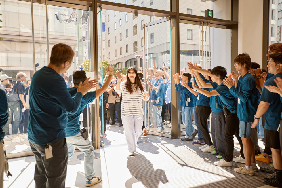 A smiling customer walks into Apple Ginza, with team members cheering.