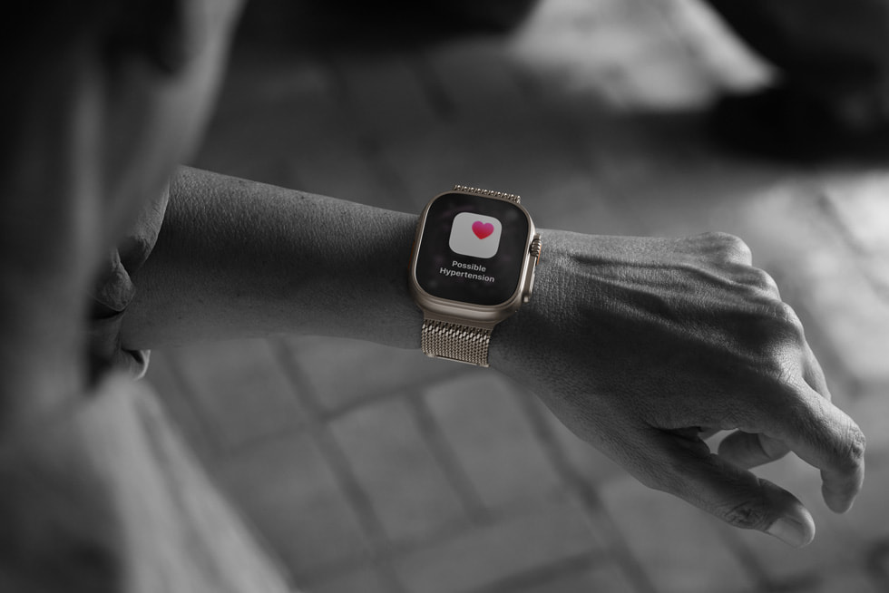 Svartvit bild av en person som tittar på sin Apple Watch Ultra 3 och ser skärmen för funktionen varningar om högt blodtryck med ett rött hjärta.
