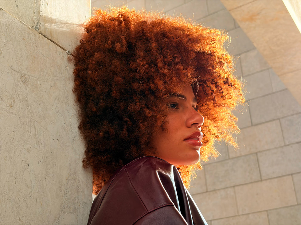 Kıvırcık saçlı bir kişinin 2 kat Telefoto özelliğiyle iPhone Air’de çekilmiş dış mekan portre fotoğrafı.