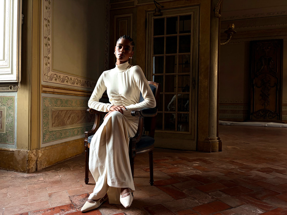 Tamamen beyaz giyinmiş, loş bir odada sandalyede oturan bir kişinin iPhone Air’de çekilmiş, bir makale için hazırlanmış gibi duran fotoğrafı.