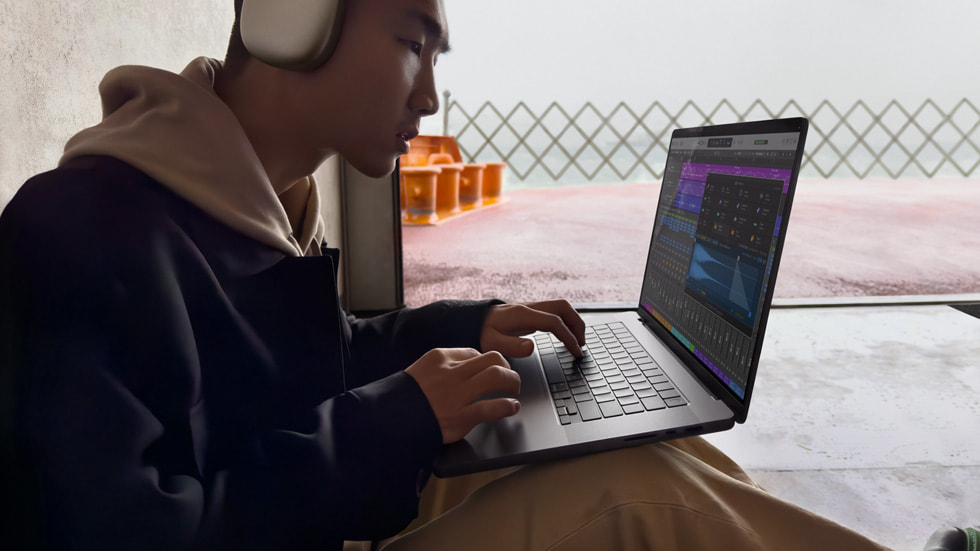 A person wearing AirPods Max working in Logic Pro on their MacBook Pro.