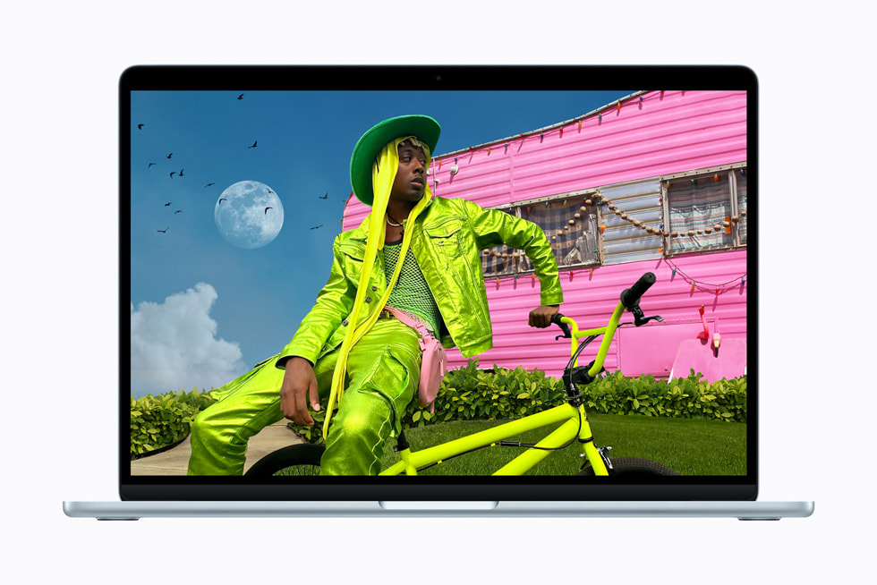 MacBook Air shows a vibrant image of a person in neon-green clothes sitting on a matching bicycle in front of a bright-pink trailer.