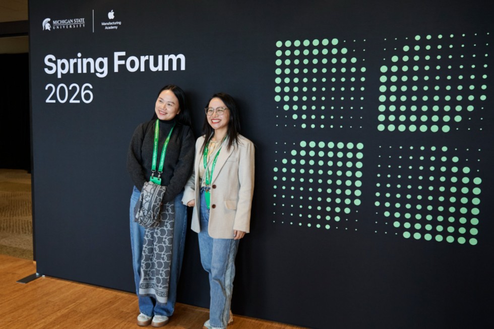 Two attendees pose in front of a wall that says “Spring Forum 2026.”