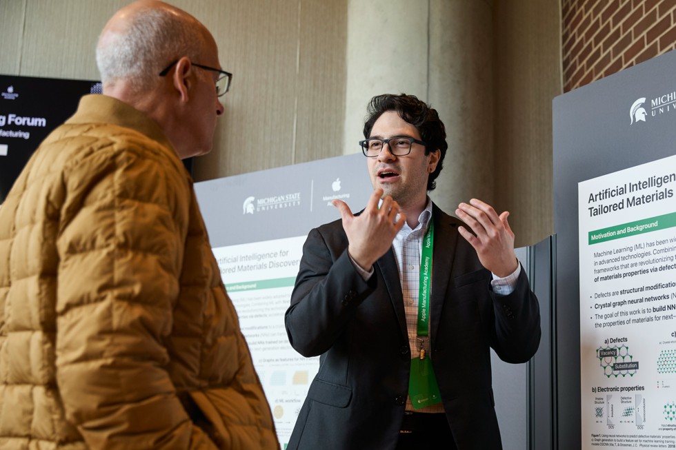 Two Spring Forum attendees are shown speaking while standing in front of a poster board with the title “Artificial Intelligence for Tailored Materials Discovery.”