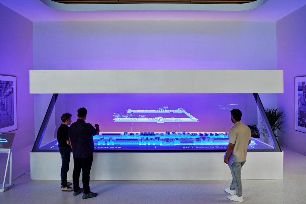 Three people stand in front of a glowing holographic table at Apple’s Advanced Manufacturing Center in Houston.