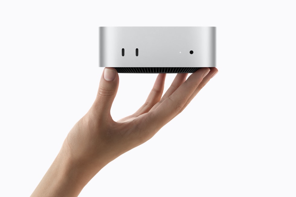 A person’s hand holds the silver Mac mini, showing its front ports.