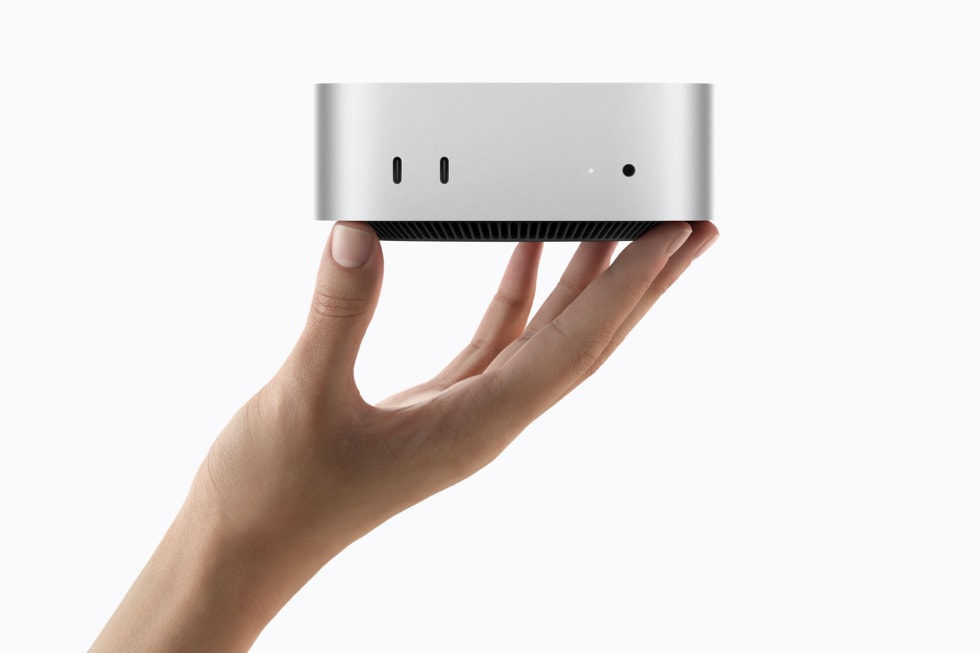 A hand holds up Mac mini against a white background.