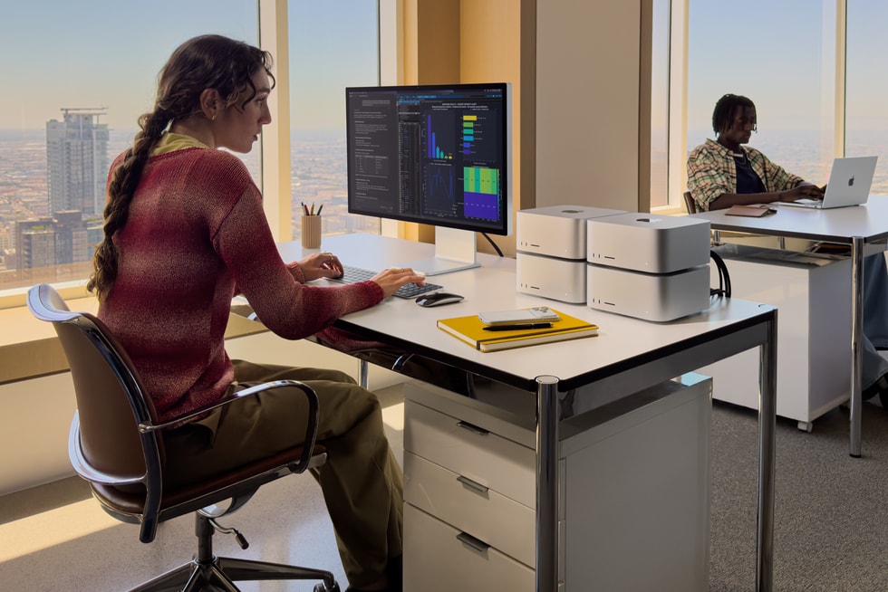 A person in an office sits in front of a desk that has a large display connected to four Mac Studio devices.