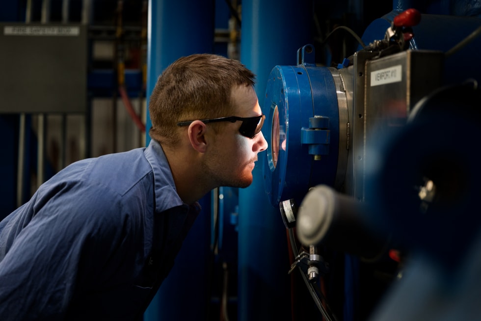 A Perryman Company employee with protective eyewear looks through a viewport.