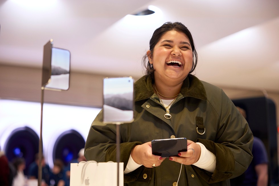 A customer holding iPhone Duo smiles next to the iPhone Duo display at Apple Fifth Avenue.