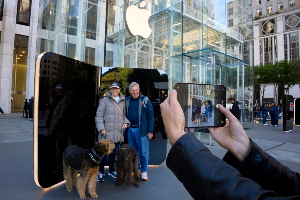 Two smiling customers and their dogs pose in front of an iPhone Duo installation outside Apple Fifth Avenue.