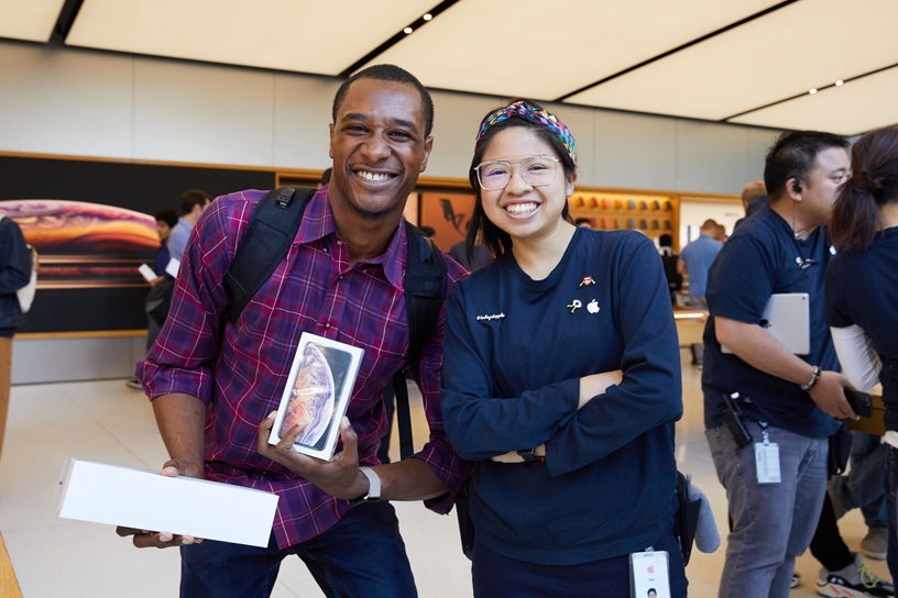 A customer holding boxes for the Apple Watch Series 4 and iPhone Xs poses for a photo with an Apple team member.