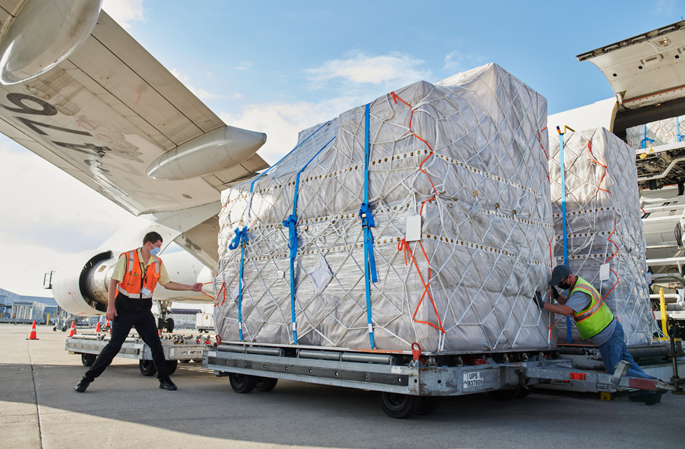 UPS Worldport employees transport palettes of iPhone 12, iPhone 12 Pro, and iPad Air shipments from an airplane. 