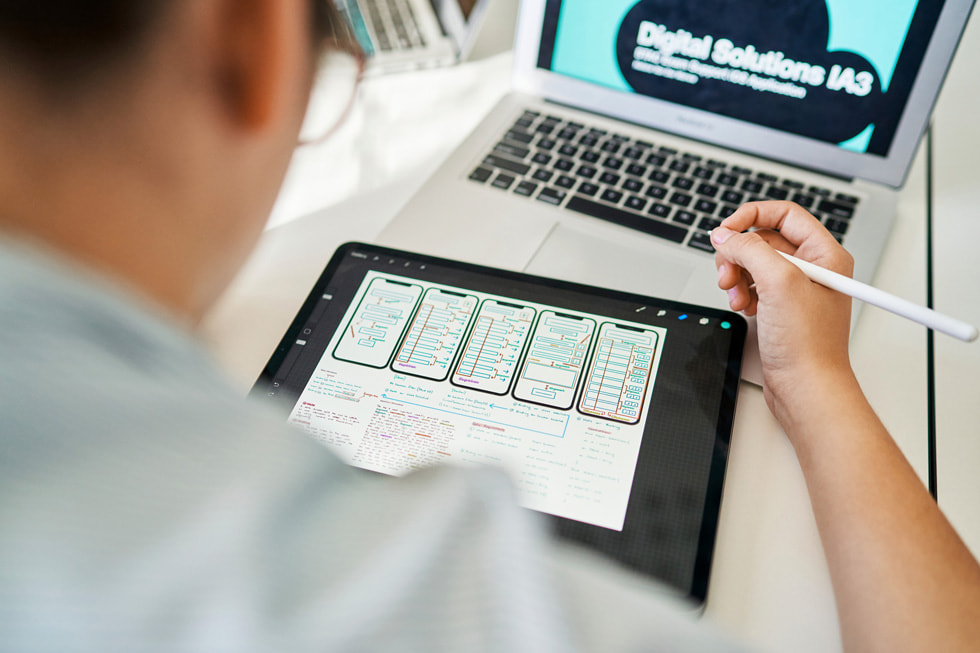 Using iPad, Apple Pencil and MacBook Air, a student works on developing an app.