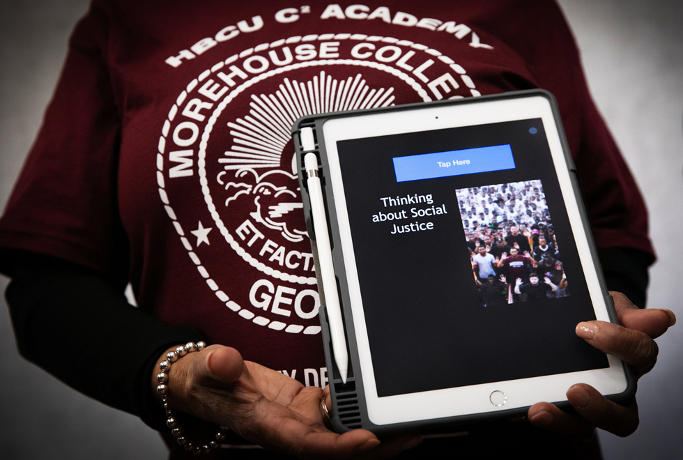 A person wearing an HBCU C2 Morehouse College sweatshirt holds an iPad Pro with the words “Thinking about social justice” displayed onscreen.