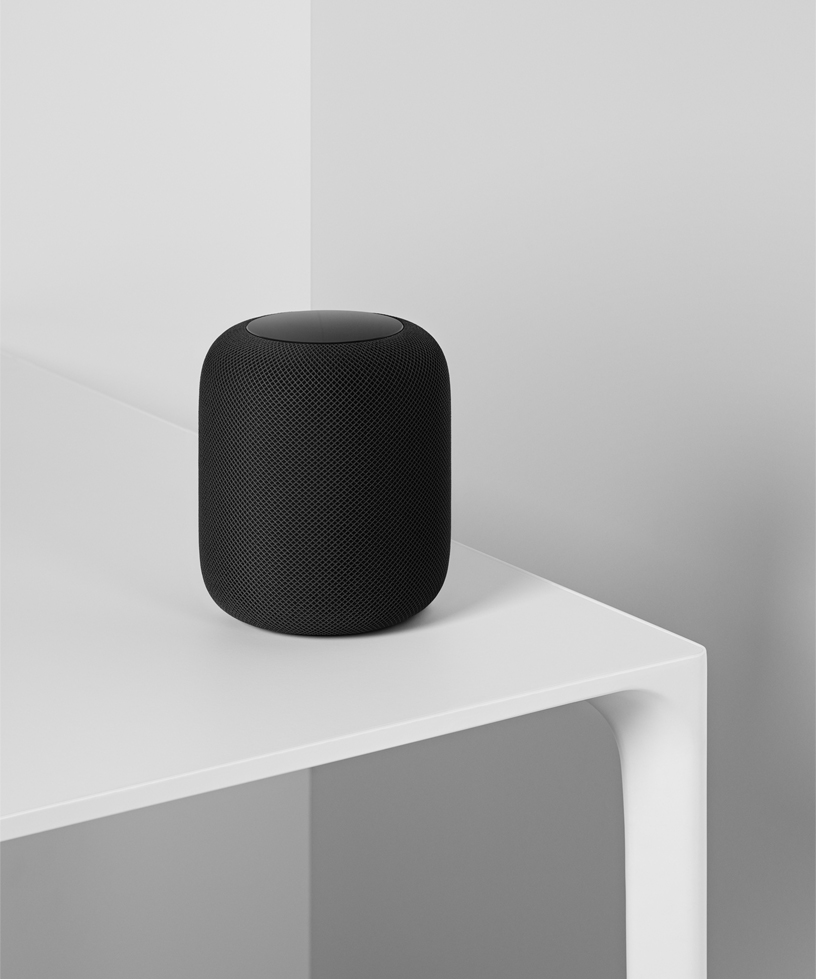 A photo of the space gray HomePod sitting on a white table.