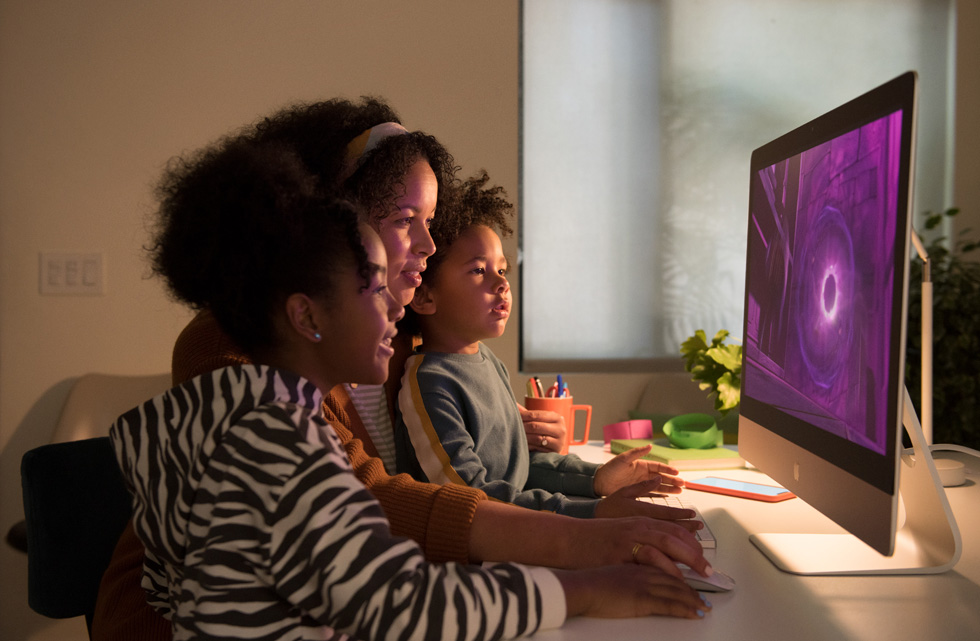A woman uses the mouse on the 27-inch iMac while two children watch the screen.