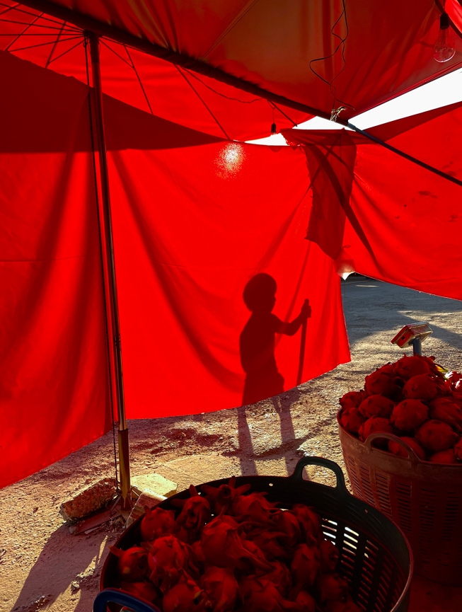 A red tarp tasked to block out the sun sets off a shadow of a child playing.