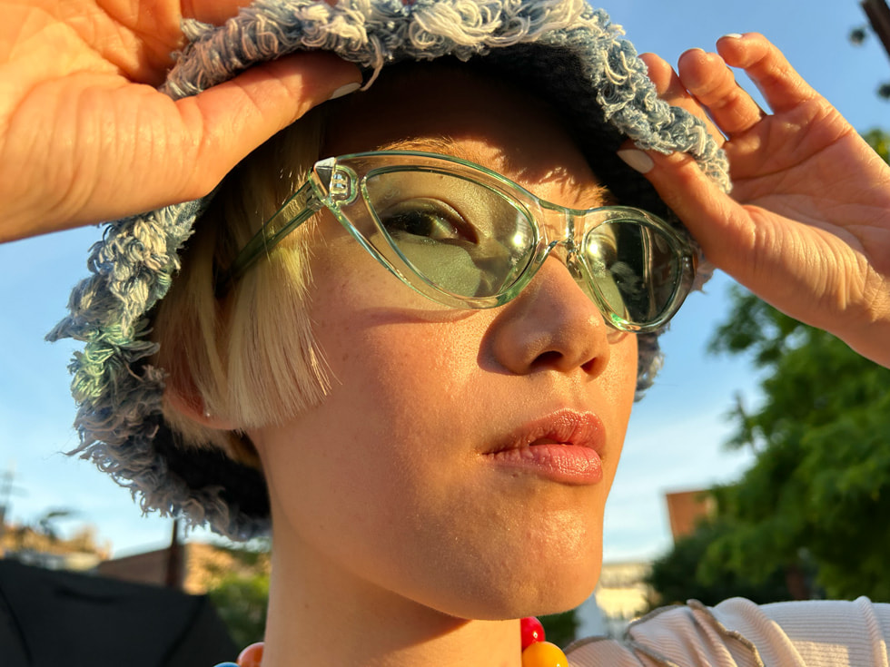 A close-up of a person wearing clear blue sunglasses and a fringed blue hat.