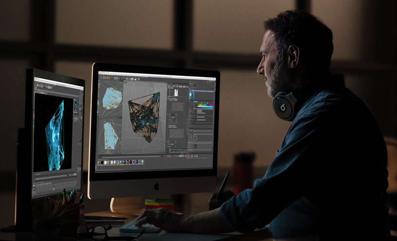 Professional reviewing 3D graphics on an iMac and additional monitor.