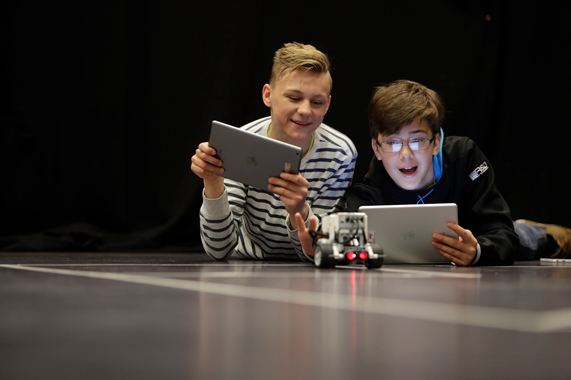 Two young people controlling a robotic car with iPads.