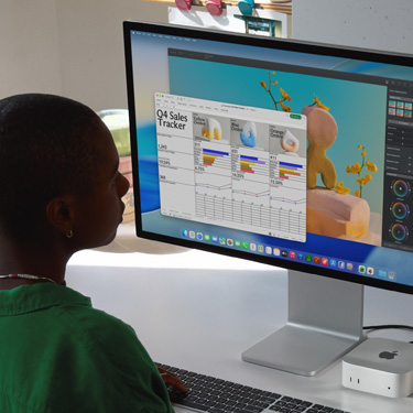 직원이 iMac과 Mac Mini로 ‘Q4 Sales Tracker’라는 제목의 Excel 스프레드시트를 작업하고 있는 모습이 보입니다. Excel 스프레드시트 뒤로는 Pixelmator Pro 창과 macOS Tahoe 배경이 보입니다.