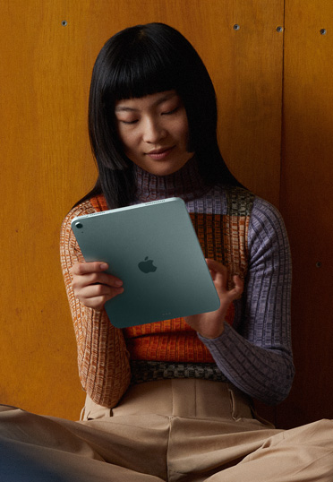 A student sitting on the floor against a wall. She’s holding an iPad.
