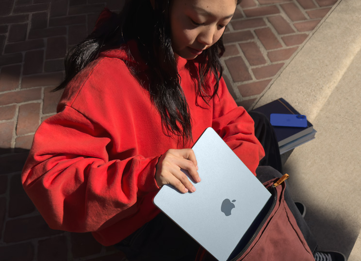 Una persona seduta su gradini di pietra che infila il MacBook nello zaino.