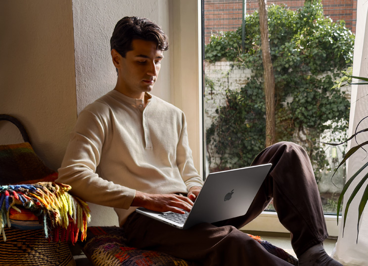 Una persona seduta sul pavimento che usa un MacBook vicino a una finestra.