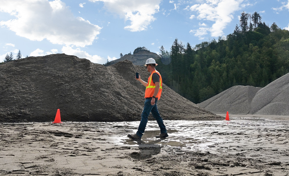 A fieldworker uses an iPhone to assess a worksite while walking across muddy terrain