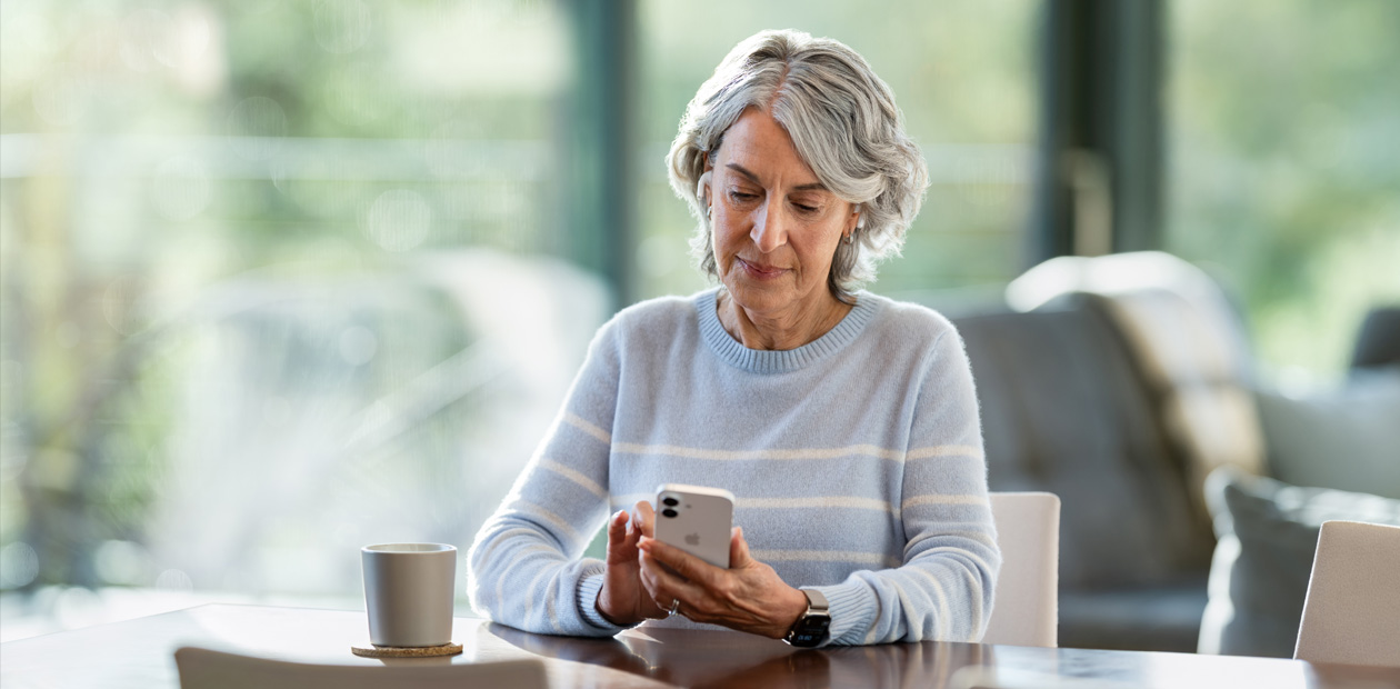 Une femme âgée assise à une table consulte un iPhone.