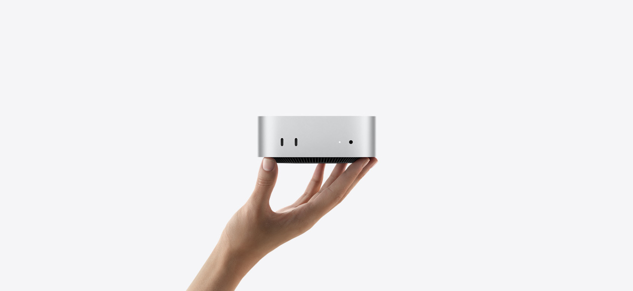 Silver Mac mini resting on a person's fingertips showing front ports and indicator light