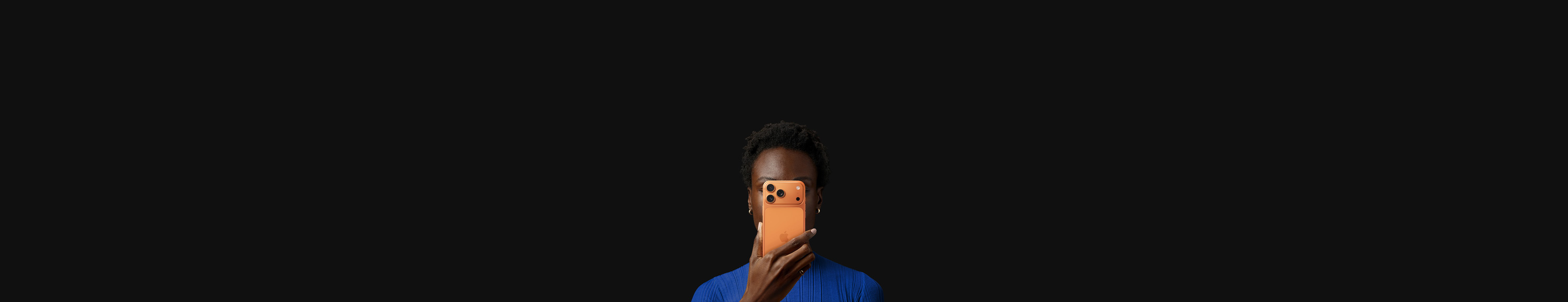 Una persona tiene iPhone 17 Pro davanti al viso, con la parte posteriore rivolta in avanti, colore arancione cosmico