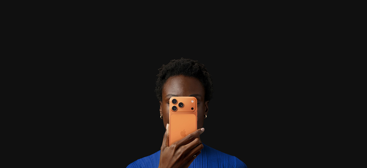 شخص يحمل iPhone&nbsp;17&nbsp;Pro أمام وجهه، الجهة الخلفية مواجهة للخارج، لون برتقالي كوني.