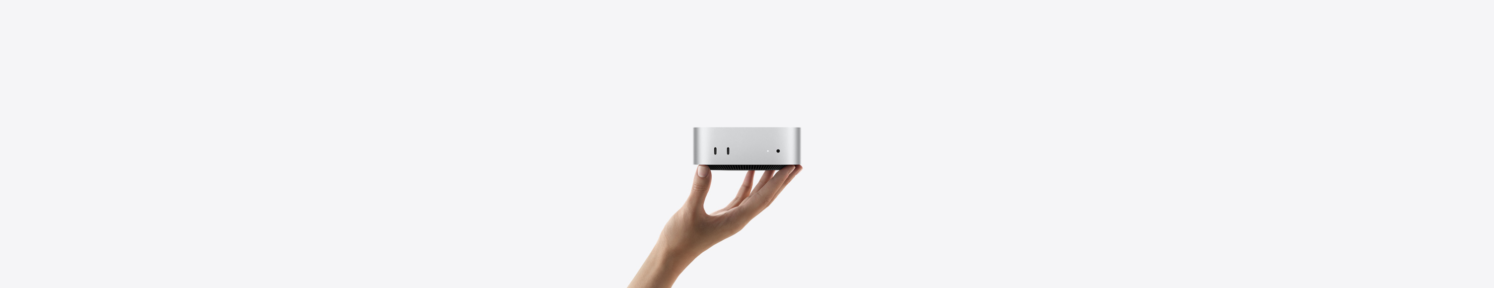 Mac mini, Vorderseite, wird auf den Fingerspitzen einer nach oben geöffneten Hand balanciert, Vorderseite mit zwei Thunderbolt Anschlüssen, Statusanzeige und 3,5 mm Kopfhöreranschluss, nach unten zulaufender schwarzer Sockel, flache Oberseite, gerundete Seiten, gerade Kanten, Farbe Silber