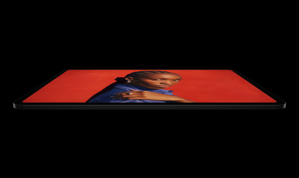 iPad Pro, parte lateral, en posición horizontal, negro espacial, esquinas redondeadas, marco de la pantalla negro, la pantalla muestra una persona con una camisa azul que posa con la mano sobre su hombro frente a un fondo rojo vibrante